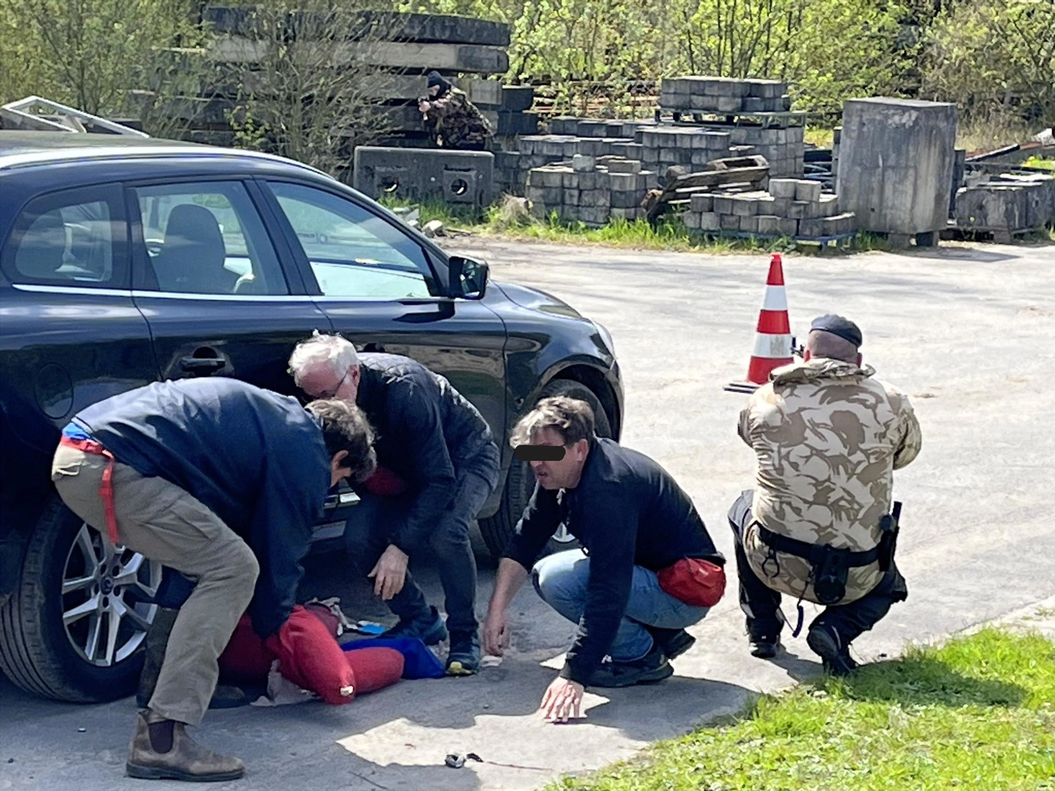 Krisenwerk GmbH - Crisis management training - Emergency responders assisting an injured person lying on the ground next to a black car. 