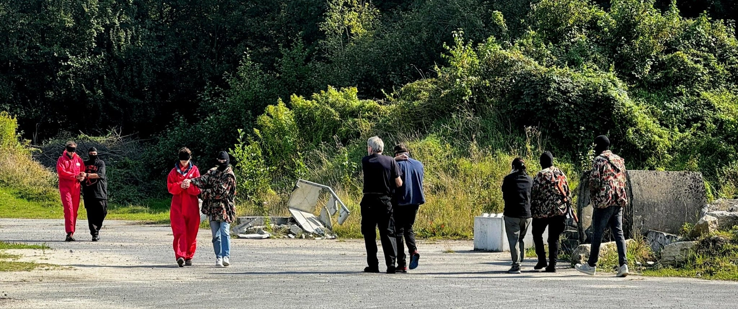 Krisenwerk GmbH - Crisis management training - A group of people in red hazmat suits and masked individuals standing on a road near greenery, with debris in the background taking them anywhere.