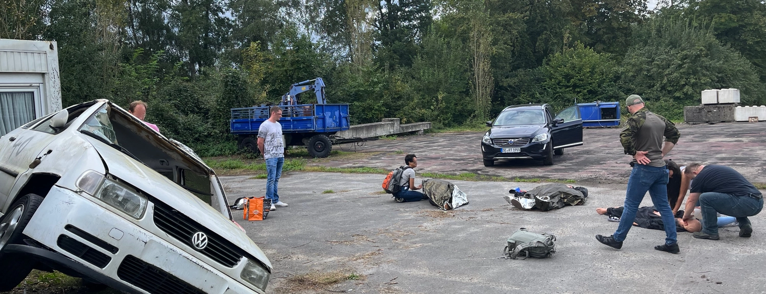 Krisenwerk GmbH - Crisis management training -  A man sitting down with bag and other are standing on the sides with cars at both sides
